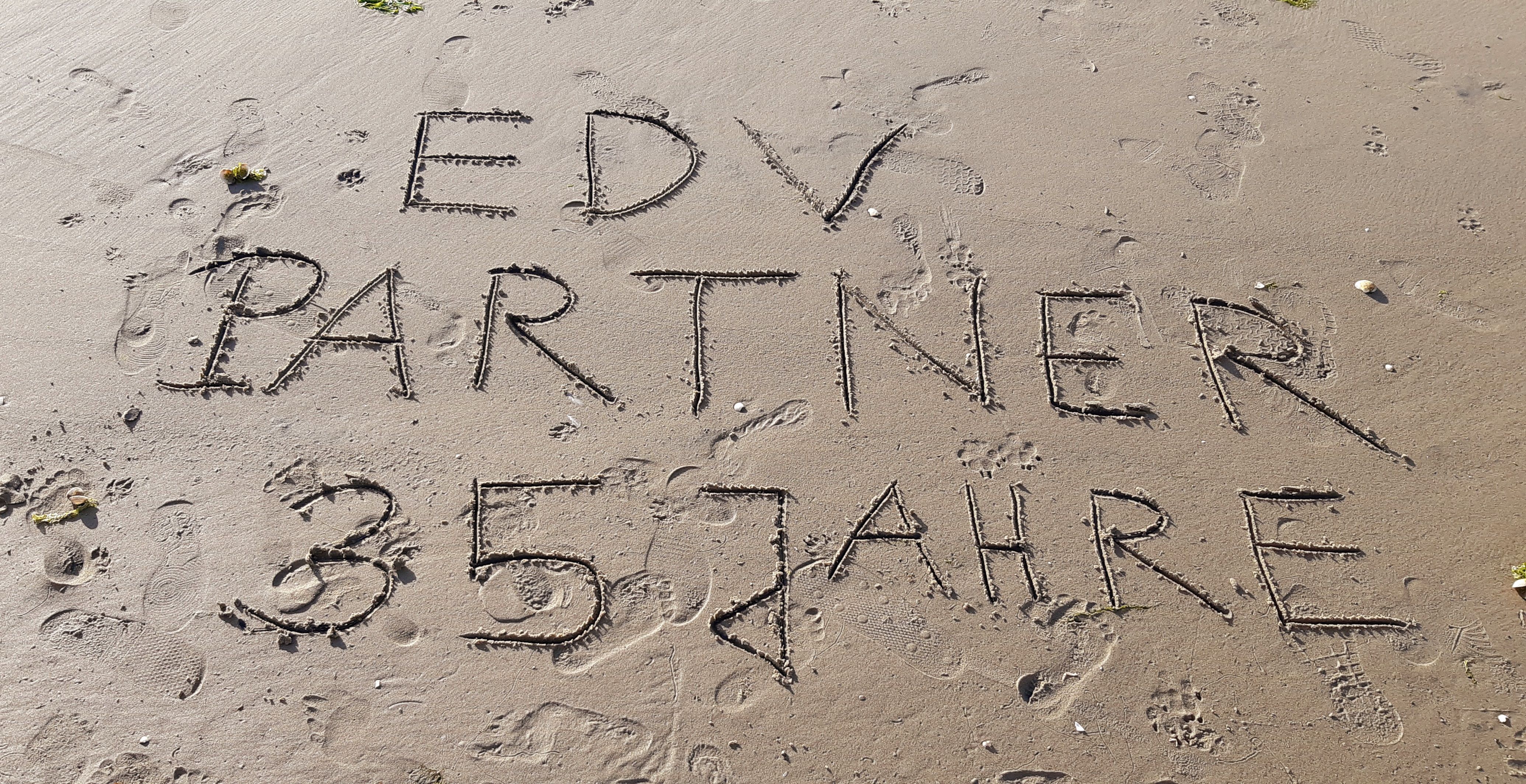 Zu sehen ist ein Foto, auf dem im feuchten Sand ‚EDV-PARTNER 35 Jahre‘ eingezeichnet ist.