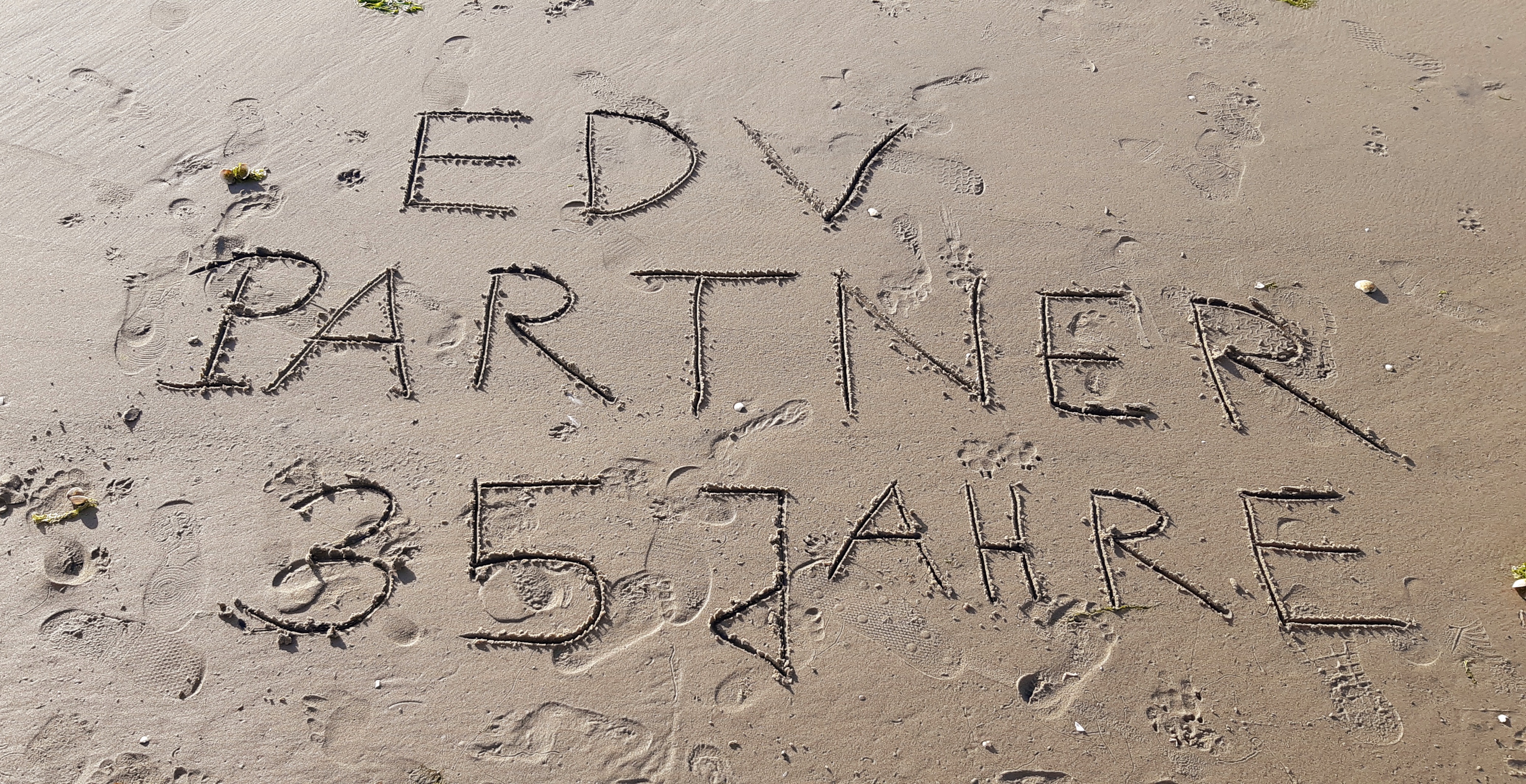 Zu sehen ist ein Foto, auf dem im feuchten Sand ‚EDV-PARTNER 35 Jahre‘ eingezeichnet ist.