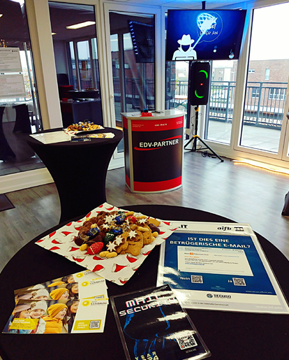 Foto von der Vorführungsbühne des Events ‚Curry 'N X-MAS‘ in der Perspektive eines Zuschauers. Zu sehen sind zusätzlich Infokarten zur Aktion Lichtblicke, zwei Hefte über Mail-Sicherheit und ein Teller voll Gebäck.