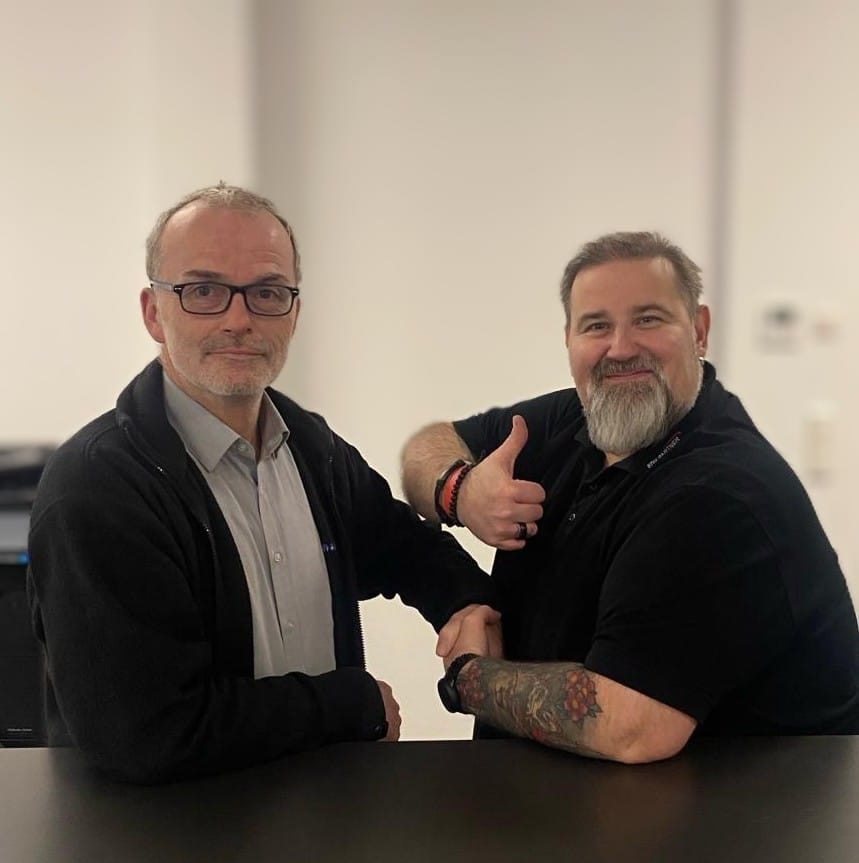 Thomas Schnieber und Thorsten Lübke, die Mitarbeiter des Jahres 2023, schütteln sich die Hand. Thorsten zeigt zusätzlich einen Daumen nach oben.