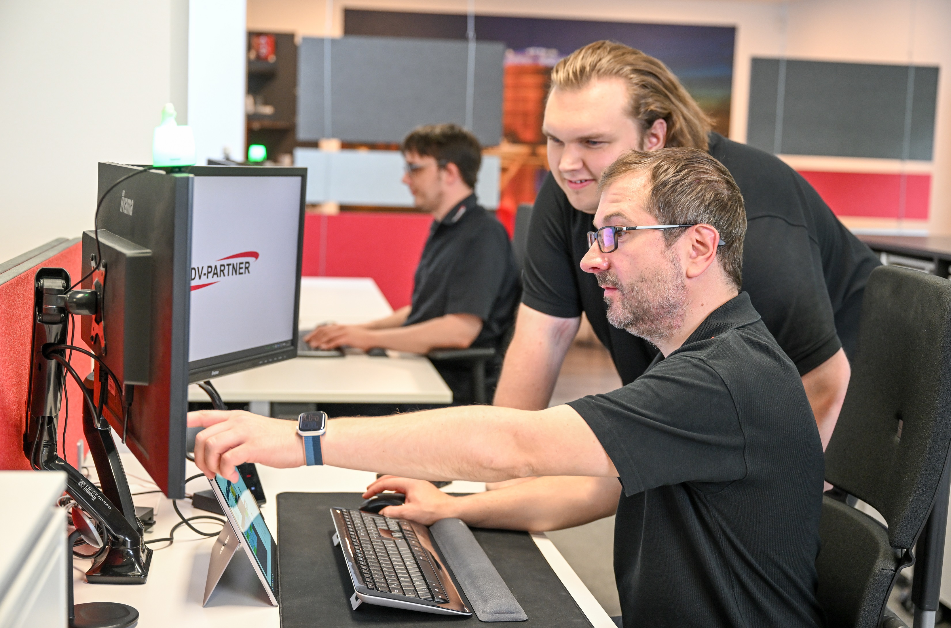 Zwei Männer im Gespräch, einer zeigt dem anderen etwas auf einem Tablet. Beide sitzen an einem Tisch mit EDV-PARTNER-Tassen.
