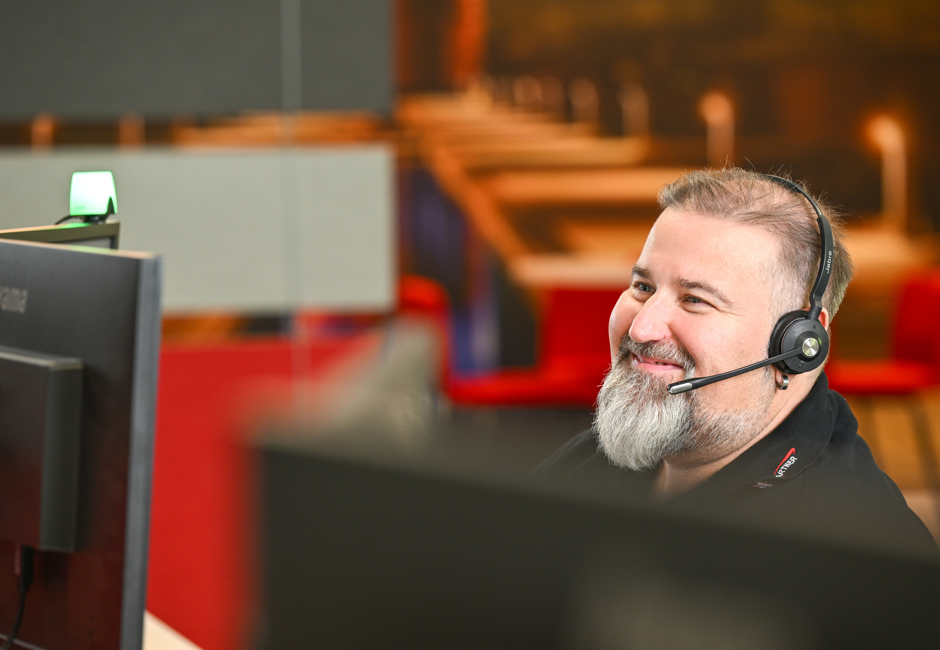 Ein Mitarbeiter lächelt freundlich, während er auf den Monitor blickt. Er trägt ein Headset und scheint sich in einem Gespräch zu befinden.