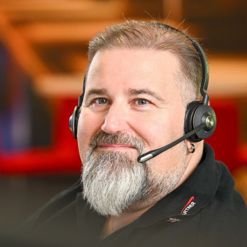 Zu sehen ist ein Mann der freundlich aber auch ernst in die Kamera schaut und ein Headset auf hat.