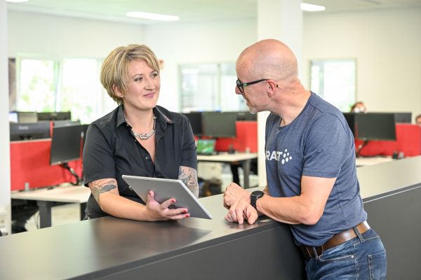 Eine Verkäuferin zeigt einem Kunden etwas auf einem Microsoft Surface und lächelt ihn dabei freundlich an.