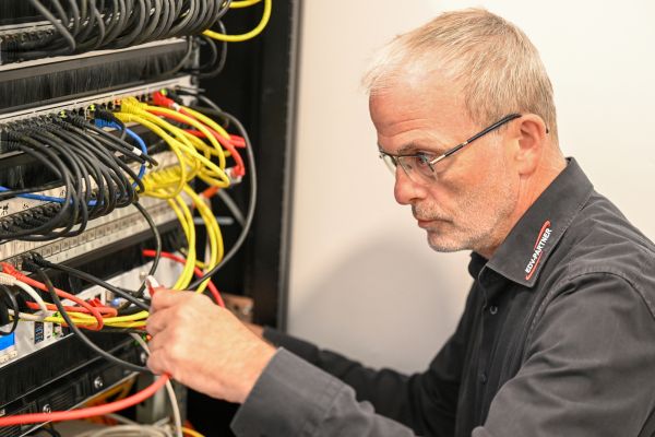 Ein IT-Techniker überprüft die Anschlüsse eines Servers und verbindet sie mit Kabeln.