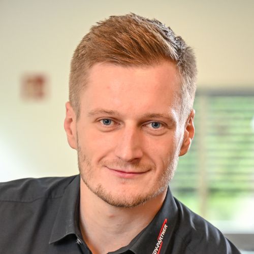 Zu sehen ist ein blonder Mann bis zur Schulterpartie, der lächelnd in die Kamera blickt.