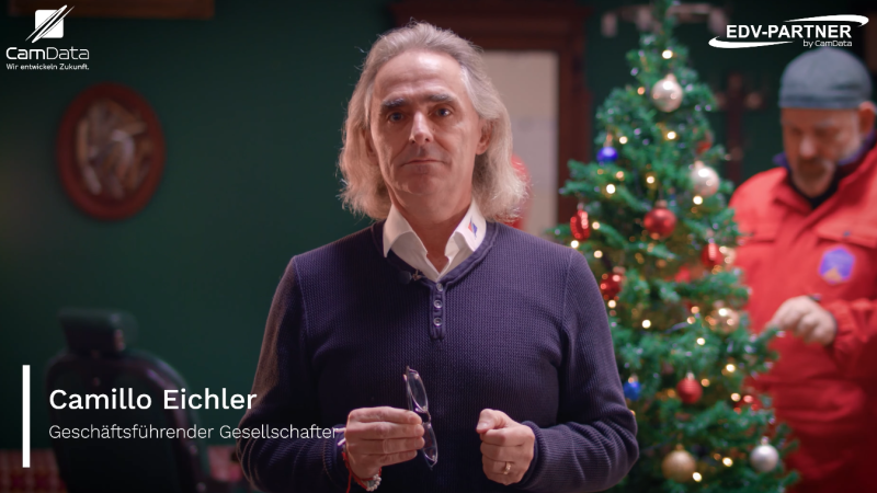 Weihnachtsmann grillt Würstchen bei einem Firmenevent, Gäste stehen zusammen, unterhalten sich und warten auf Essen.