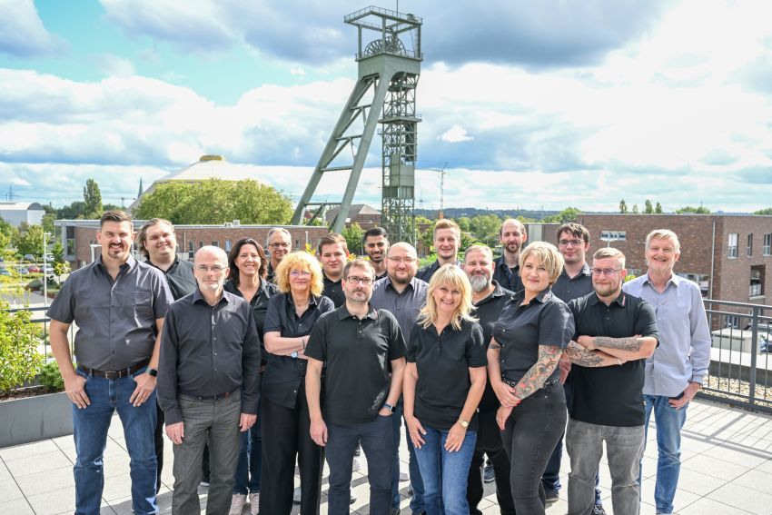 Gruppenfoto aller Mitarbeitenden der EDV-PARTNER GmbH. Im Hintergrund sind ein Förderturm und ein leicht bewölkter Himmel zu sehen.